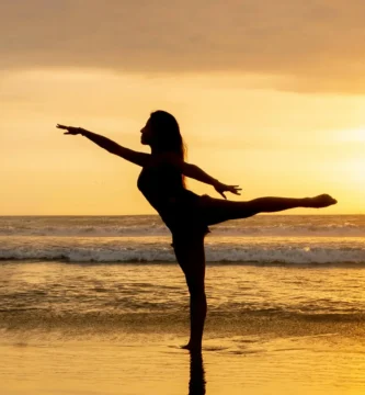 Mujer practicando posturas de yoga de pie frente al mar