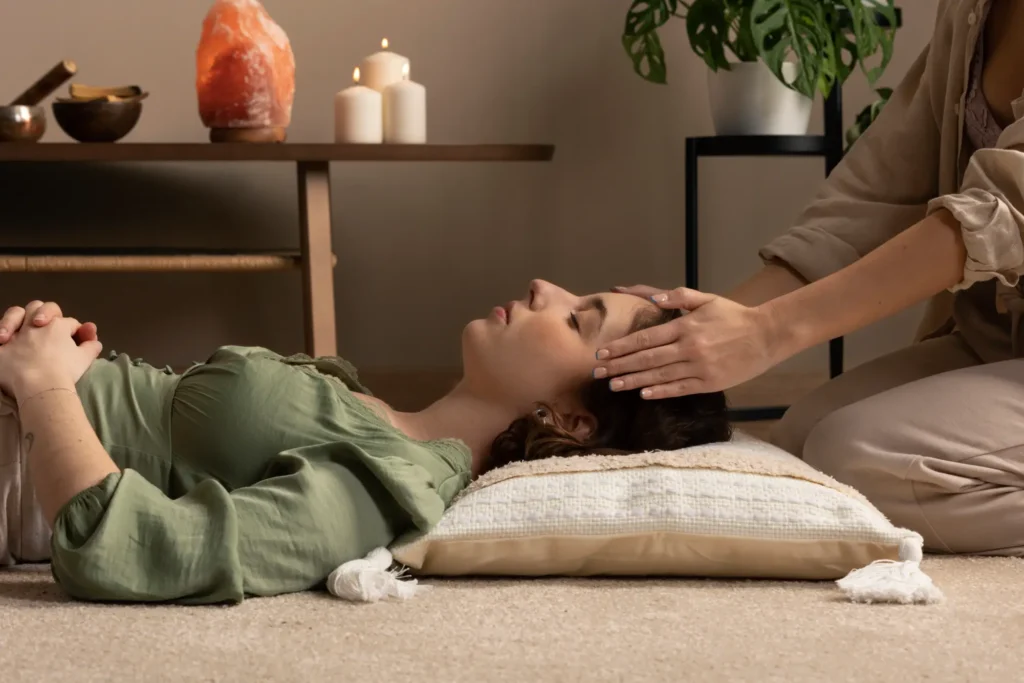 Mujer recibiendo sesión de Reiki en la frente para liberar estrés y equilibrar su energía en un entorno relajante con velas y decoración natural.