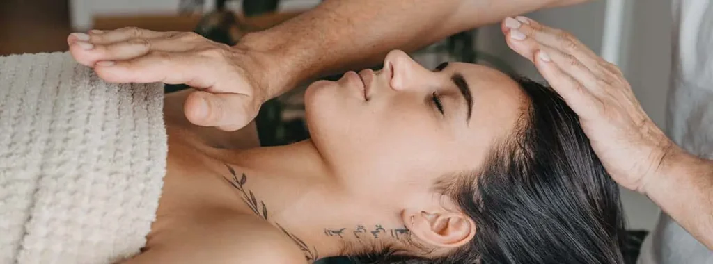 Terapia Reiki con imposición de manos sobre una mujer recostada, relajada y con los ojos cerrados.