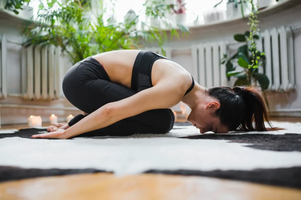 Mujer practicando Balasana o postura del niño en yoga, una asana restaurativa para relajar la espalda y reducir el estrés