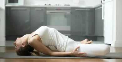 Mujer practicando la postura de la diosa reclinada Supta Baddha Konasana en casa sobre una esterilla de yoga.