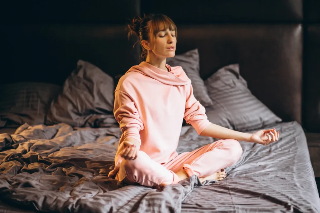 Mujer joven realizando secuencia de yoga en cama para reducir el estrés y dormir mejor.