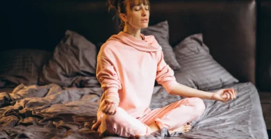Mujer joven realizando secuencia de yoga en cama para reducir el estrés y dormir mejor.
